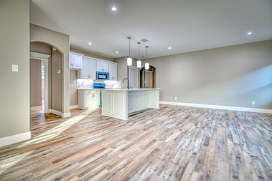 Kitchen with arched walkways, recessed lighting, hanging light fixtures, a kitchen island with sink, and white cabinets