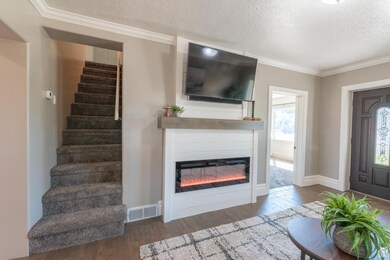 Entryway featuring dark wood-style floors, a textured ceiling, crown molding, a glass covered fireplace, and stairway
