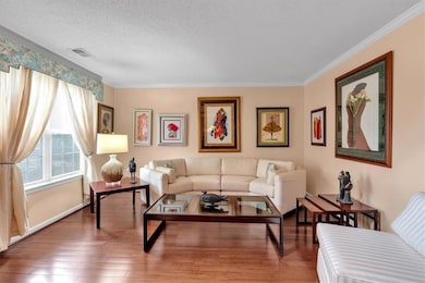 Living room featuring a textured ceiling, ornamental molding, wood finished floors, and baseboards