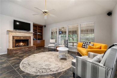 Living area featuring a fireplace, lofted ceiling, a ceiling fan, and dark stone finish floors