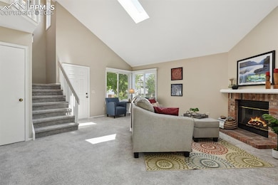 Living area featuring high vaulted ceiling, stairway, a fireplace, carpet floors, and a skylight