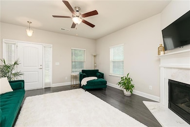 Living area with ceiling fan, dark wood-style floors, and a high end fireplace