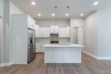 Kitchen featuring white cabinetry, stainless steel appliances, hanging light fixtures, a center island with sink, and light wood-style floors