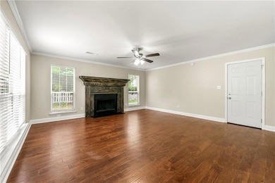 Unfurnished living room with a ceiling fan, dark wood-style floors, healthy amount of natural light, a fireplace with flush hearth, and ornamental molding