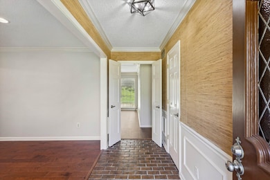 Hall with crown molding, brick floors, a textured ceiling, wooden walls, and baseboards