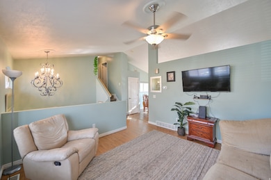 Living room with wood finished floors, a chandelier, vaulted ceiling, and a ceiling fan