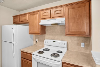 Kitchen featuring white appliances, under cabinet range hood, light countertops, and brown cabinets