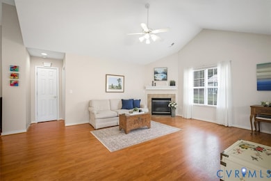 Living room with light wood-style flooring, a tiled fireplace, ceiling fan, and high vaulted ceiling