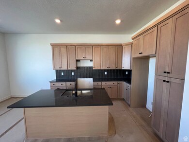 Kitchen with tasteful backsplash, a center island with sink, dark stone countertops, a textured ceiling, and recessed lighting