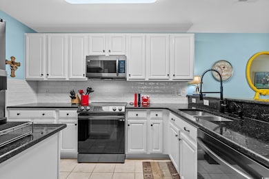 Kitchen with appliances with stainless steel finishes, white cabinets, light tile patterned floors, dark stone countertops, and backsplash