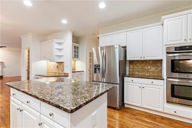 Kitchen with appliances with stainless steel finishes, open shelves, crown molding, tasteful backsplash, and white cabinets