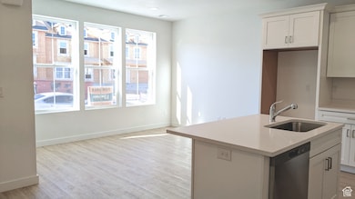 Kitchen with stainless steel dishwasher, light wood-style flooring, a kitchen island with sink, and white cabinets (pictures are of a previous home built)