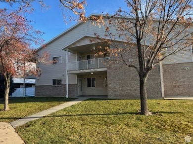 Rear view of house with a yard, brick siding, and a balcony