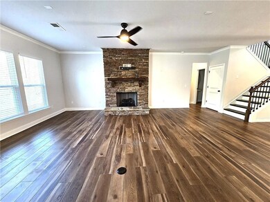 Unfurnished living room featuring stairway, a stone fireplace, ornamental molding, dark wood-type flooring, and ceiling fan