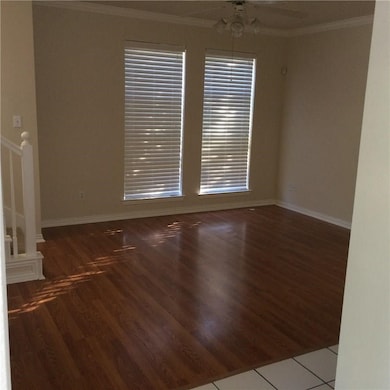 Empty room featuring ornamental molding, wood finished floors, a ceiling fan, and stairs