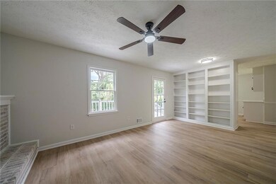 Unfurnished living room with a textured ceiling, ceiling fan, light wood-style floors, baseboards, and built in features