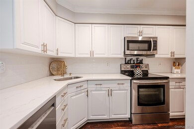 Kitchen featuring stainless steel appliances, white cabinets, decorative backsplash, light stone countertops, and crown molding