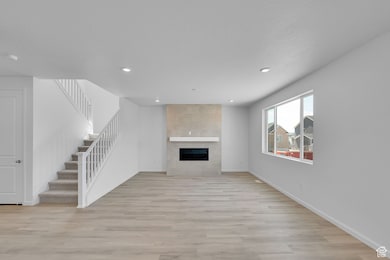 Unfurnished living room with light wood-type flooring, a tile fireplace, recessed lighting, and stairs