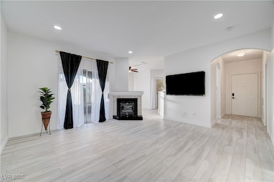 Unfurnished living room with a glass covered fireplace, recessed lighting, arched walkways, light wood finished floors, and a ceiling fan