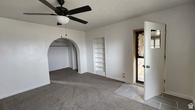 Carpeted empty room featuring baseboards, ceiling fan, built in shelves, arched walkways, and tile patterned flooring