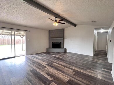 Unfurnished living room featuring dark wood-type flooring, ceiling fan, lofted ceiling with beams, a textured ceiling, and a brick fireplace