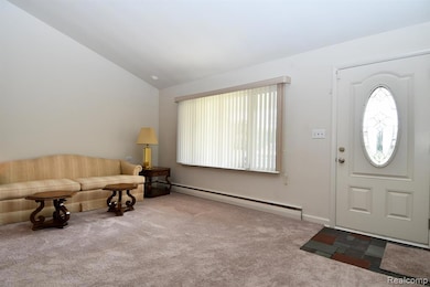 Carpeted foyer entrance featuring baseboard heating and vaulted ceiling