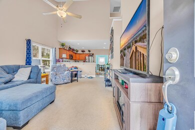 Living area featuring a ceiling fan, light colored carpet, and a towering ceiling