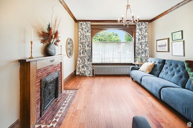 Living room featuring ornamental molding, radiator, a chandelier, hardwood / wood-style floors, and a brick fireplace
