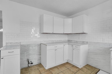 Kitchen with tile walls, a textured ceiling, light countertops, light tile patterned flooring, and white cabinets