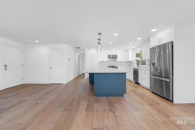 Kitchen featuring appliances with stainless steel finishes, a center island, light wood finished floors, light countertops, and white cabinetry