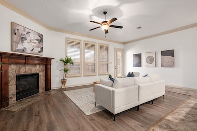 Living room featuring ornamental molding, a ceiling fan, a fireplace, and wood finished floors
