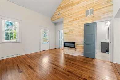 Unfurnished living room with high vaulted ceiling, healthy amount of natural light, wood-type flooring, a large fireplace, and wood walls