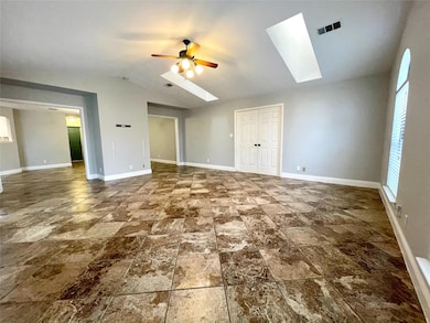 Unfurnished living room with a skylight, a ceiling fan, lofted ceiling, plenty of natural light, and stone finish floors