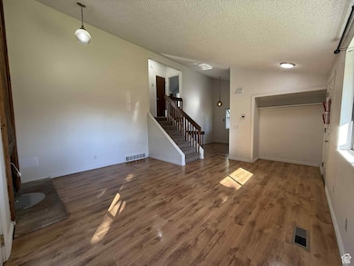 Unfurnished living room with wood finished floors, a textured ceiling, vaulted ceiling, and stairway