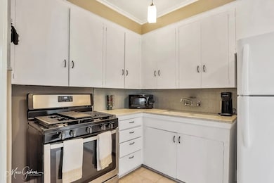 Kitchen featuring freestanding refrigerator, stainless steel range with gas stovetop, white cabinets, decorative backsplash, and crown​​‌​​​​‌​​‌‌​​‌​​​‌‌​​​​​​‌‌‌​​‌​​‌‌​​​‌ molding