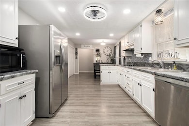 Kitchen featuring appliances with stainless steel finishes, white cabinets, a peninsula, light wood-style flooring, and tasteful backsplash