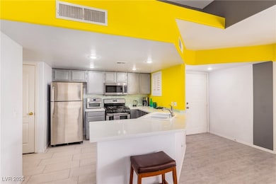 Kitchen with appliances with stainless steel finishes, a peninsula, light countertops, a breakfast bar, and gray cabinets