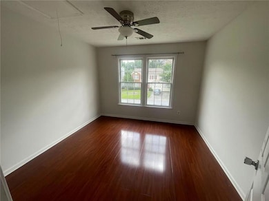 Empty room with attic access, dark wood-style floors, a textured ceiling, and a ceiling fan