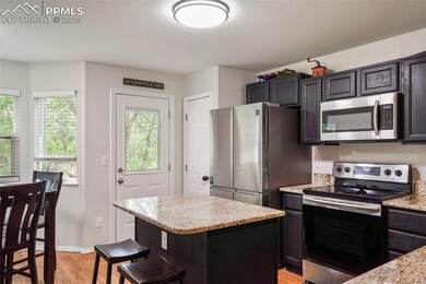 Kitchen with stainless steel appliances, light wood-style floors, a kitchen island, light stone countertops, and a breakfast bar area