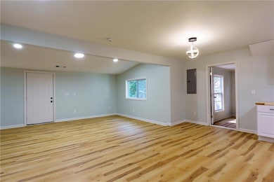Unfurnished room featuring light wood finished floors, vaulted ceiling, electric panel, and recessed lighting