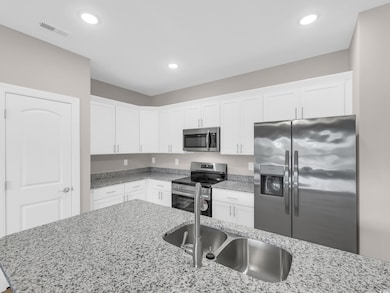 Kitchen with stainless steel appliances, white cabinetry, light stone countertops, and recessed lighting