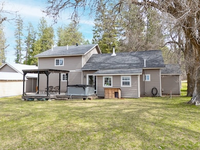 Back of house featuring roof with shingles, a pergola, a hot tub, a yard, and a deck