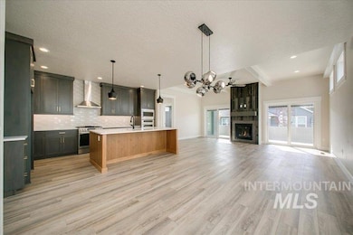 Kitchen with appliances with stainless steel finishes, wall chimney range hood, open floor plan, light countertops, and tasteful backsplash