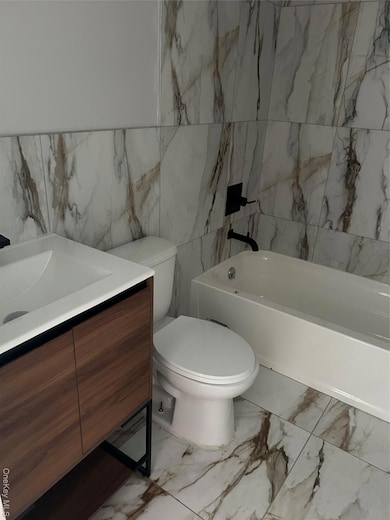 Bathroom featuring tile walls, light marble finish flooring, vanity, and a bath