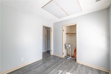 Unfurnished bedroom featuring a closet, baseboards, attic access, and wood finished floors