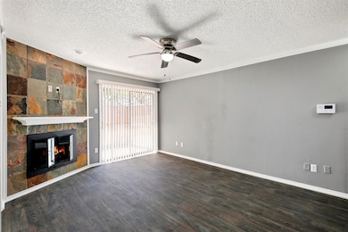 Unfurnished living room featuring a tiled fireplace, dark wood-type flooring, a textured ceiling, and ceiling fan