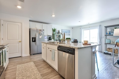 Kitchen featuring white cabinetry, appliances with stainless steel finishes, light stone counters, a breakfast bar, and recessed lighting