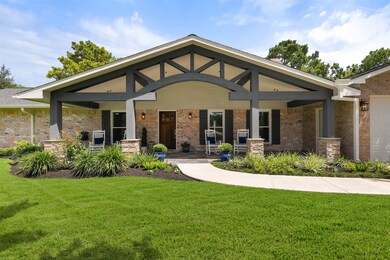An extra-long paved driveway leads from Falling Leaf Drive amidst the towering trees that dot this property to this charming single-story home with ample parking space and a brick elevation with wood shutters and the most inviting gabled front porch.