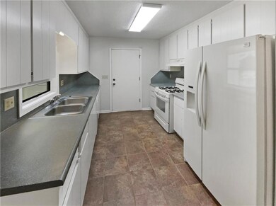 Kitchen with white appliances, white cabinetry, under cabinet range hood, dark countertops, and dark stone finish flooring
