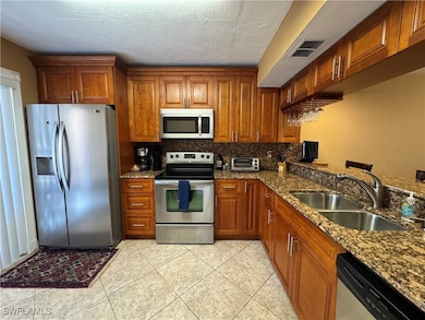 Kitchen featuring brown cabinetry, visible vents, appliances with stainless steel finishes, a sink, and decorative backsplash